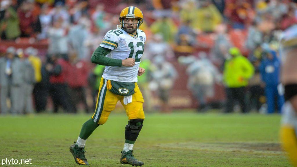 Aaron Rodgers smiling and waving to fans during a pre-game warm-up.